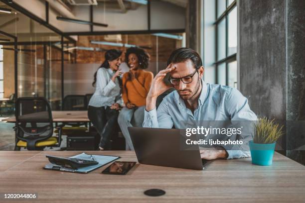 positieve multi-etnische werknemers die over vermoeide mannelijke collega roddelen - bully stockfoto's en -beelden