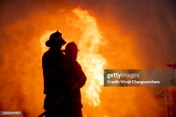 silhouette of two firefighter in front of the big fire, fire insurance concept - brandstiftung stock-fotos und bilder