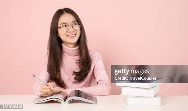 learning and education concept. back to school education knowledge college university concept. beautiful female college student holding her pen smiling happily sitting at desk on pink background - examination table bildbanksfoton och bilder