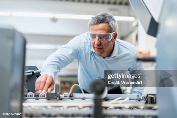 man wearing safety goggles adjusting a machine in a factory - printing stock-fotos und bilder