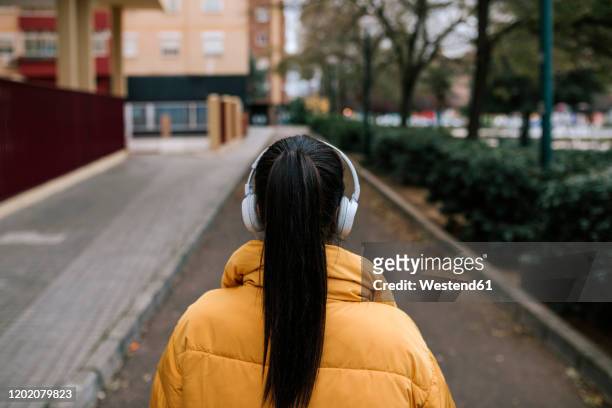 back view of woman with black hair listening music with headphones on the street - puffer jacket photos et images de collection
