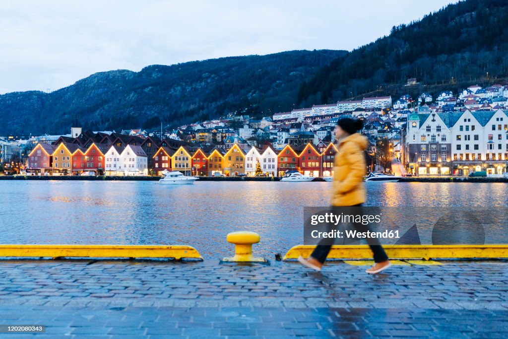Woman wearing a yellow jacket and walking at harbour in Bergen, Norway
