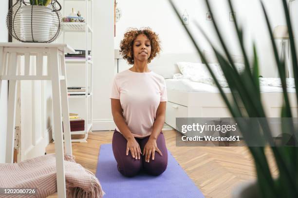 young woman practicing yoga at home - woman kneeling stock-fotos und bilder