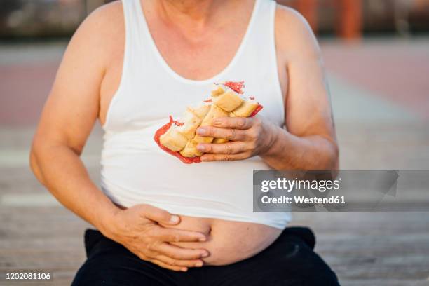 man with beer belly holding sandwich - carne procesada fotografías e imágenes de stock