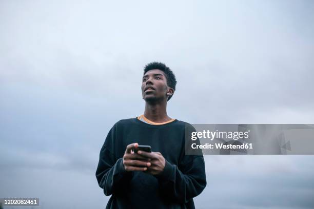 teenager using his smartphone, low angle view - black teenager stock-fotos und bilder