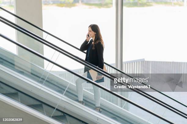 smiling businesswoman on escalator talking on the phone - escalator side view stock pictures, royalty-free photos & images