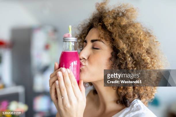 woman kissing a smoothie glass at home - frau locken beauty nicht draußen stock-fotos und bilder
