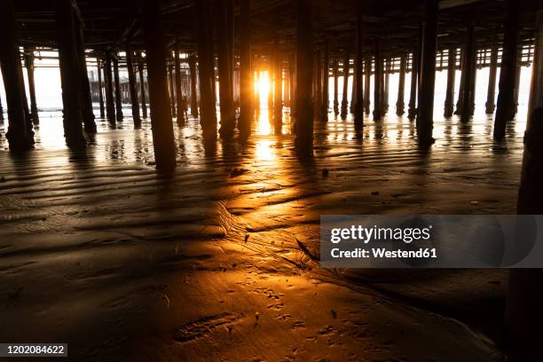 usa, california, santa monica, setting sun illuminating beach sand under santa monica pier - santa monica pier stock-fotos und bilder