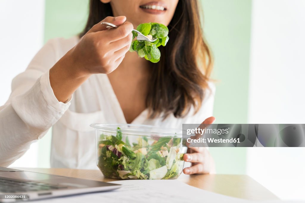 Crop view of young architect eating mixed salad at desk