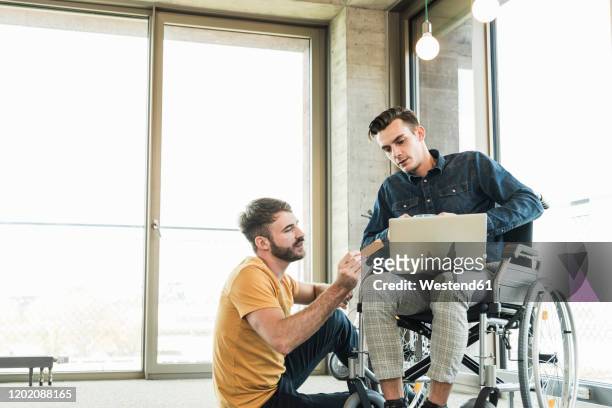 young businessman in wheelchair and colleague using laptop in office - dedication stock pictures, royalty-free photos & images