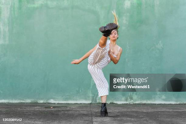 young woman doing a high kick in front of green wall - verteidigen stock-fotos und bilder