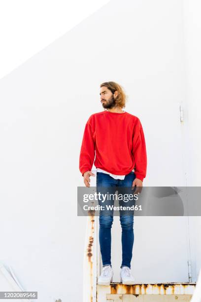 portrait of bearded young man wearing red sweatshirt standing on rusty stairs - looking around on white background stock pictures, royalty-free photos & images