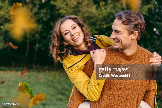 man giving woman a piggyback ride outdoors in autumn - versierd jak stockfoto's en -beelden