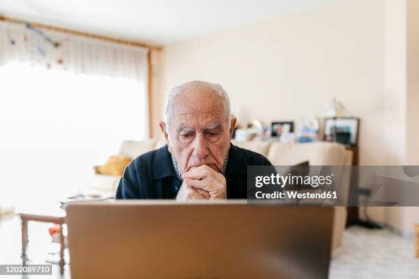 portrait of senior man using laptop at home - teleurstelling stockfoto's en -beelden