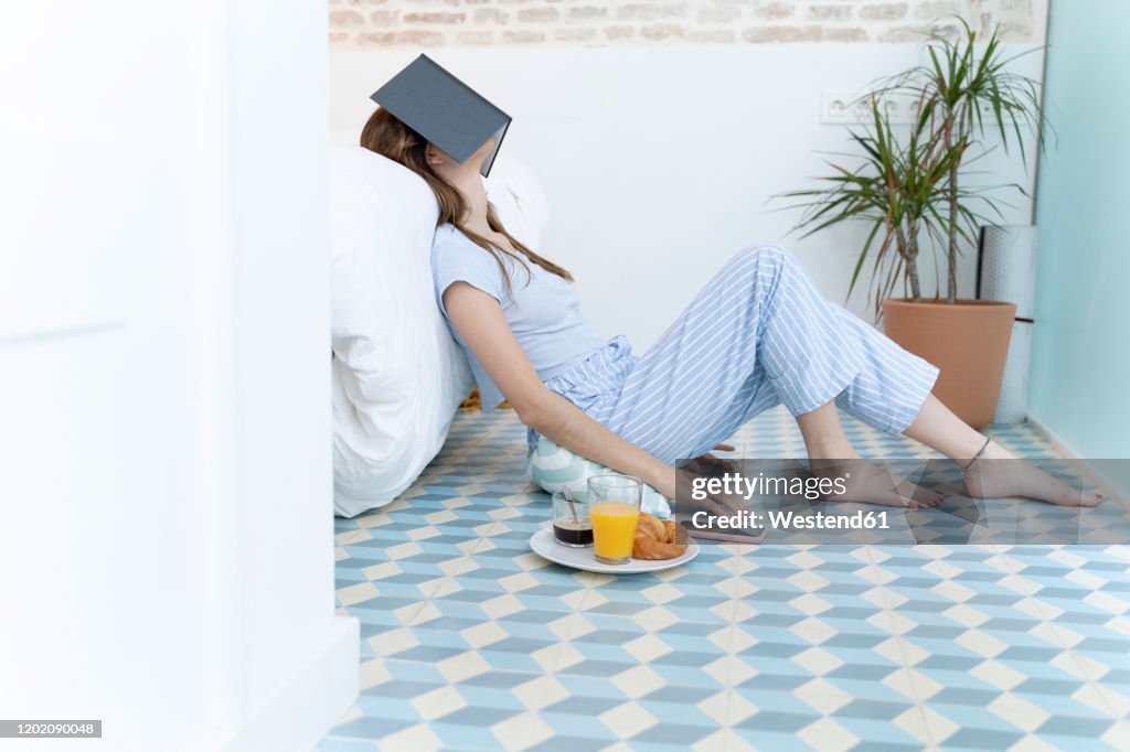 Young woman sitting on the floor and a book on her head in bedroom