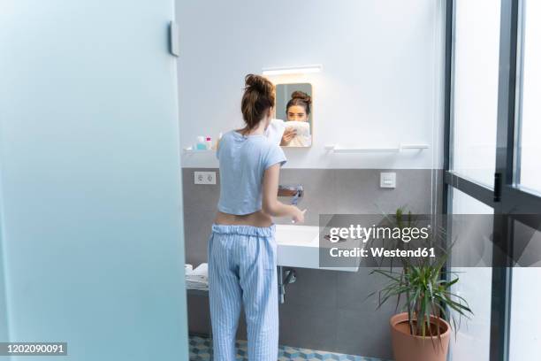 rear view of young woman brushing teeth in bath room - brush teeth phone stock-fotos und bilder