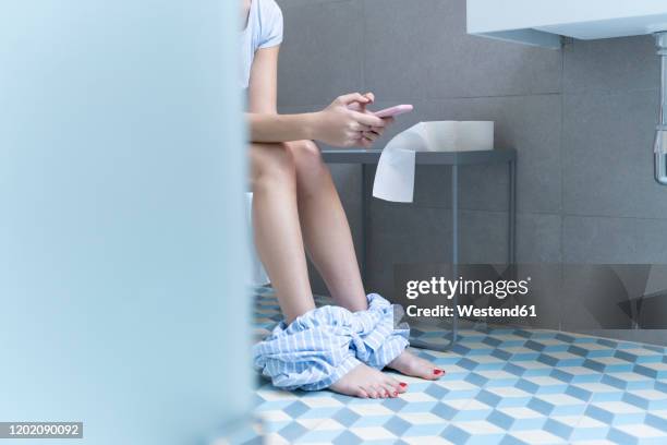 young woman sitting on toilet and using smartphone - men taking a dump stockfoto's en -beelden