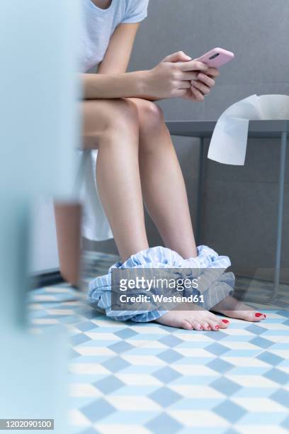young woman sitting on toilet and using smartphone - women in slips stock-fotos und bilder