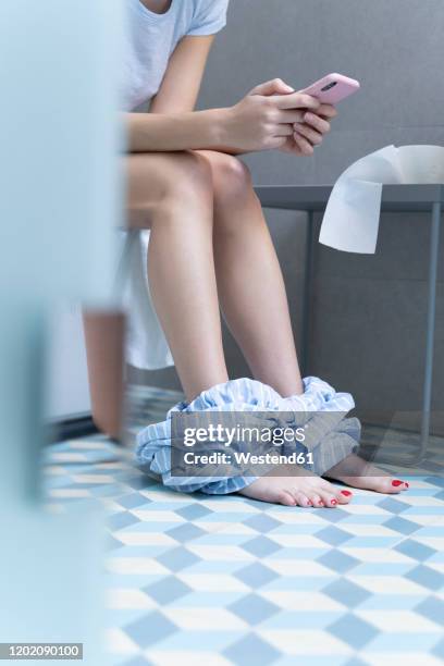 young woman sitting on toilet and using smartphone - human toilet 個照片及圖片檔