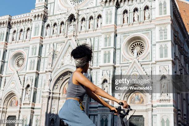 young woman riding bicycle in front of cathedral, florence, italy - florence ストックフォトと画像