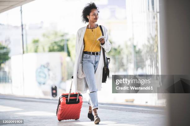 young woman with cell phone and earphones at the train station - woman suitcase stock pictures, royalty-free photos & images