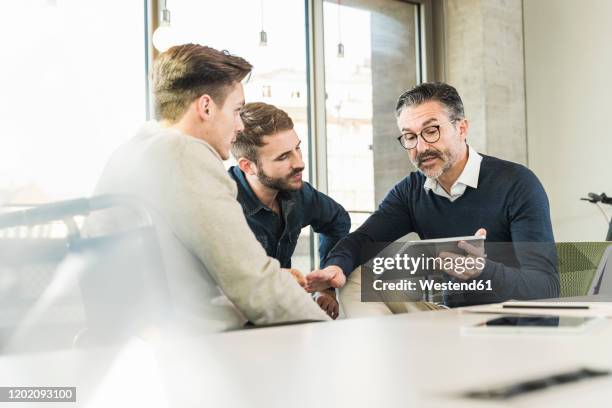 three businessmen having a meeting in office sharing a tablet - dedication stock-fotos und bilder