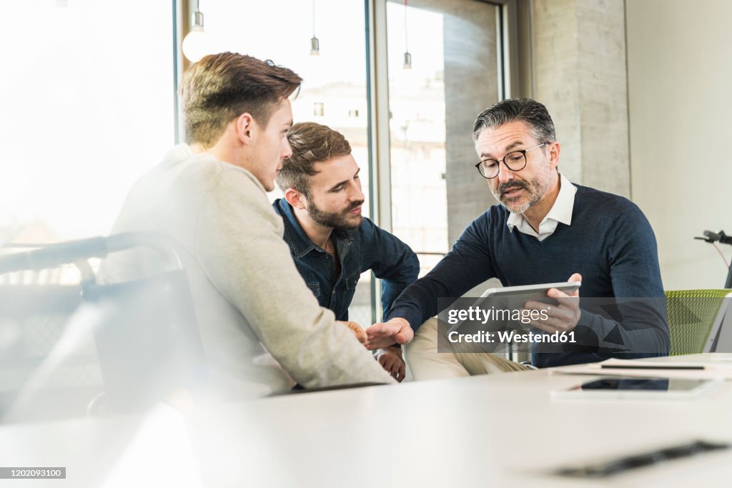 Three businessmen having a meeting in office sharing a tablet