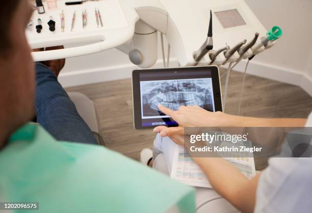 female dentist explaining patient's x-ray image on digital tablet - dentist office foto e immagini stock