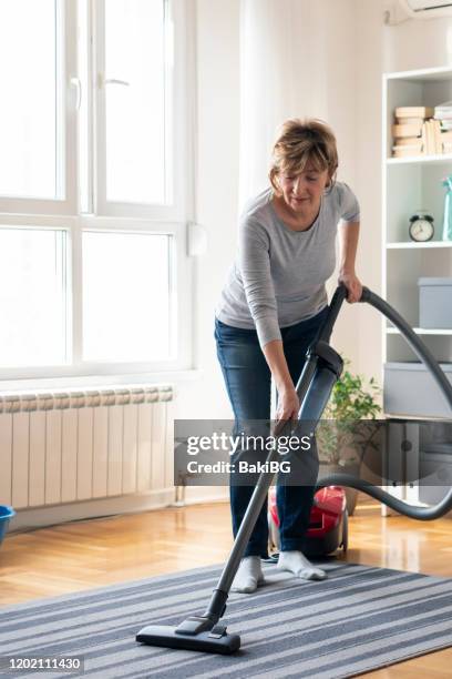 mujer mayor limpiando alfombras con una aspiradora en casa - vacuum cleaner fotografías e imágenes de stock