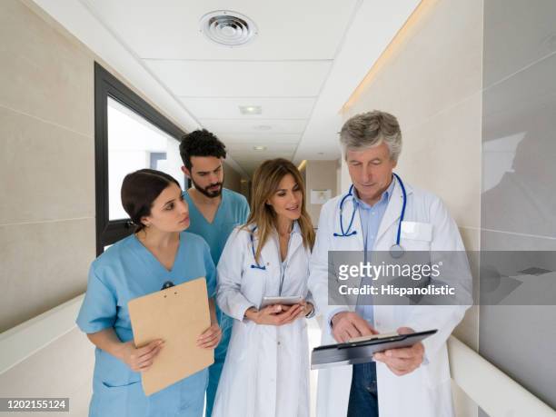 senior doctor talking to his team of interns while pointing something on clipboard at the hospital - resident stock pictures, royalty-free photos & images