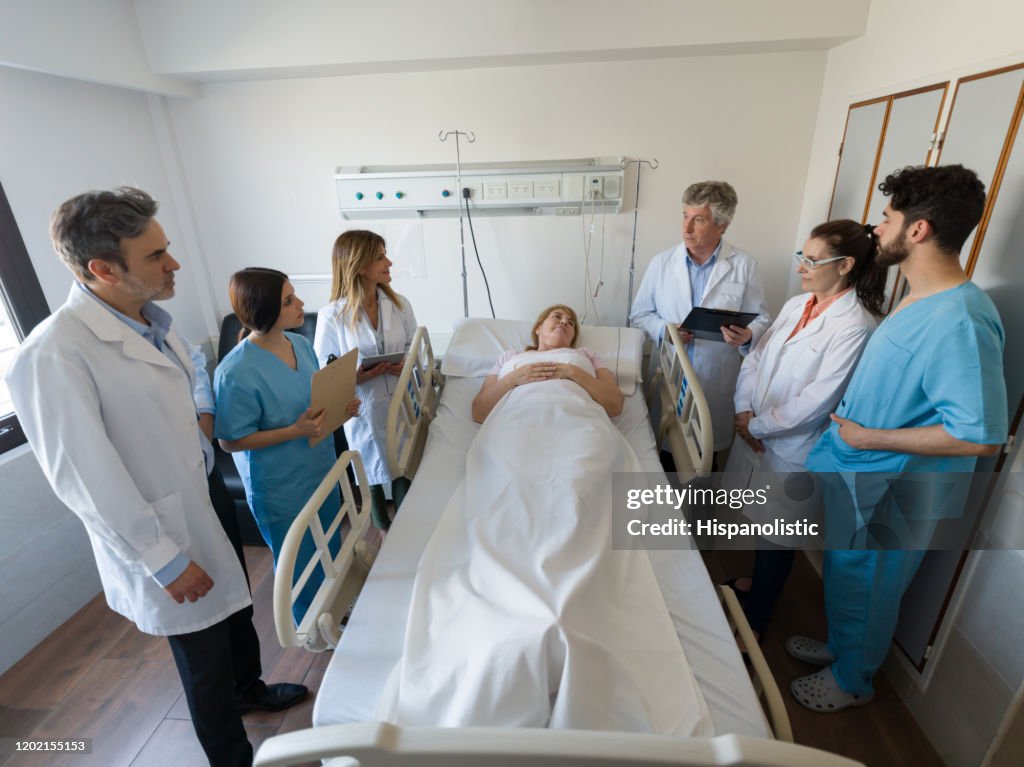 Equipo de residentes médicos, enfermera y médico de alto rango visitando a una paciente hospitalizada de alto rango hablando con ella