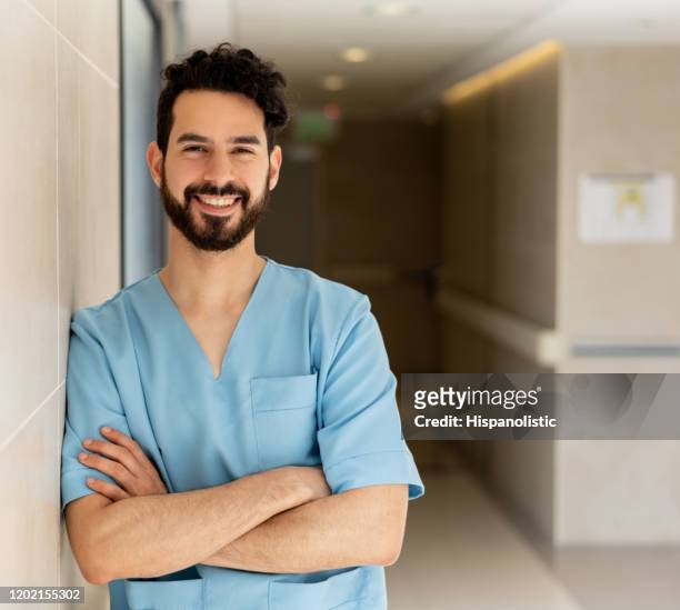 friendly medical resident at the hospital leaning against the wall with arms crossed smiling at camera - civilian stock pictures, royalty-free photos & images