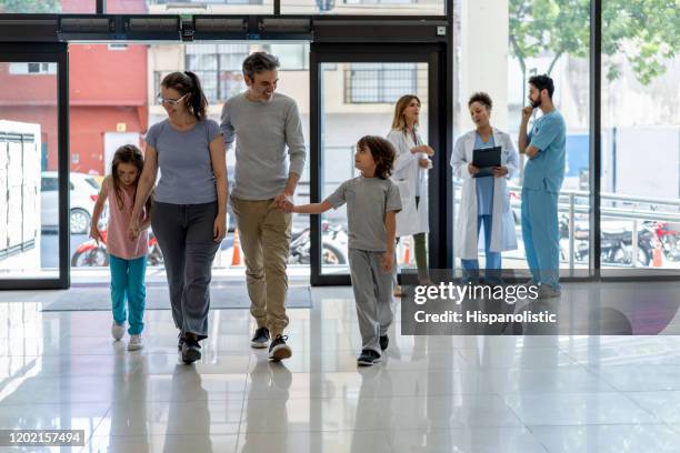 glückliche familie mit zwei kindern, die für einen termin mit dem kinderarzt ins krankenhaus gehen - krankenhaus eingang stock-fotos und bilder