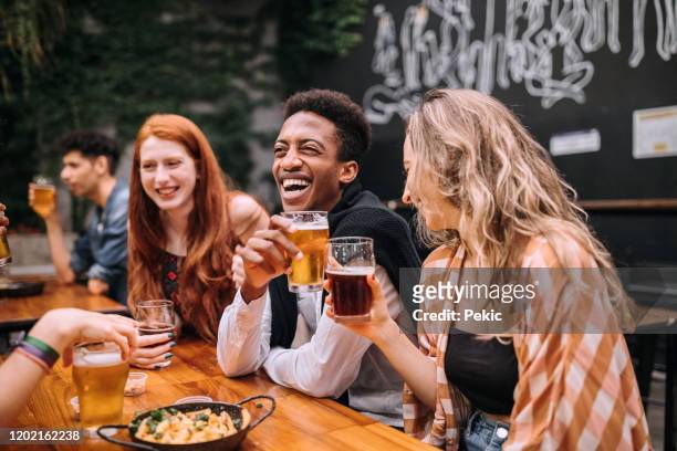 multi-ethnic group of hipster people sitting at table in brewery and having a few beers - outdoor brewery stock pictures, royalty-free photos & images