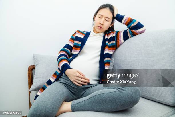a pregnant woman suffering from sickness while sitting on couch - morning sickness stockfoto's en -beelden