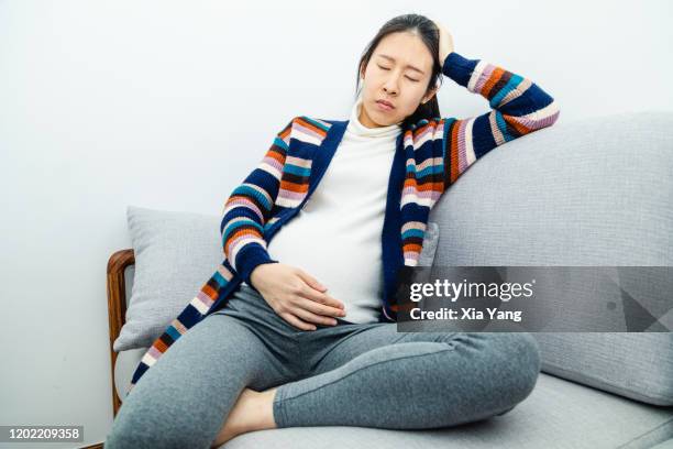 a pregnant woman suffering from sickness while sitting on couch - morning sickness - fotografias e filmes do acervo