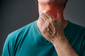 Unhappy Asian man using his hand touching on his neck Suffering From Gland Inflammation. Adult man feels bad on a sore throat and sick from cold, flu. Throat pain, sickness, healthcare, and medical concept.