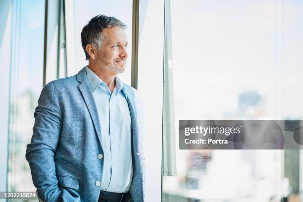 confident businessman looking through window - business man contemplating stock pictures, royalty-free photos & images