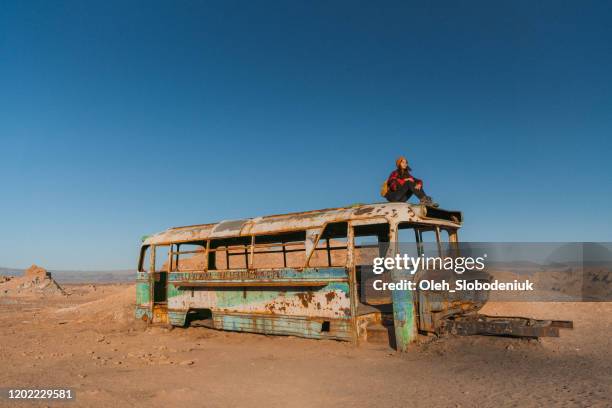 frau sitzt auf dem dach eines verlassenen busses in der atacama-wüste - san pedro de atacama stock-fotos und bilder