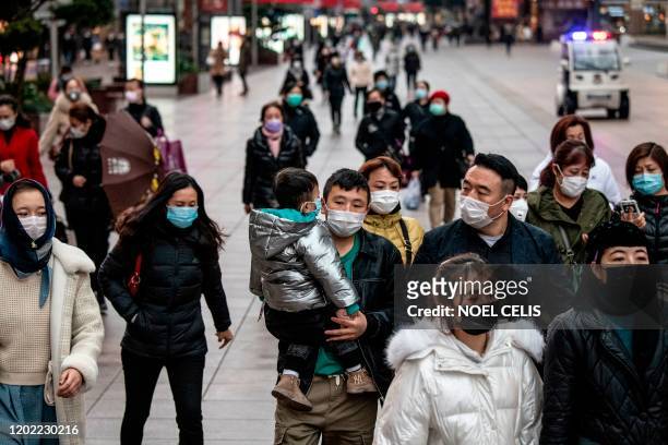 People wearing protective facemasks walk along a street in Shanghai on February 21, 2020. - Two more people died from the new coronavirus in Iran,...