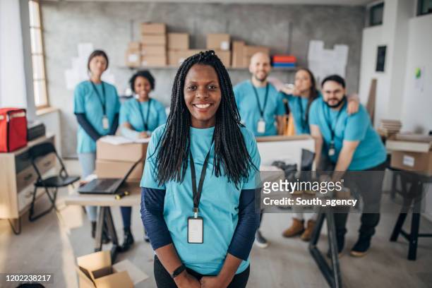 black woman with volunteers friends in charity food bank - charity and relief work stock pictures, royalty-free photos & images