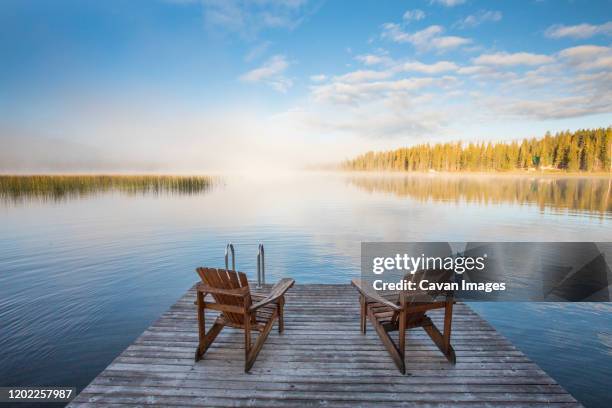 wooden chairs on dock looking over lake at dawn - adirondack chair stock pictures, royalty-free photos & images