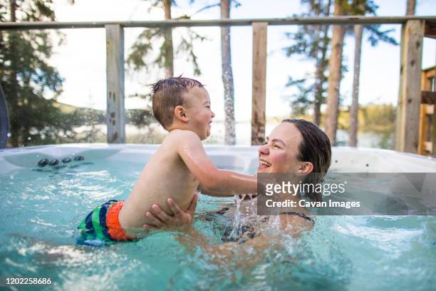 young boy splashing and playing with mother in swimming pool - girls in hot tub stockfoto's en -beelden