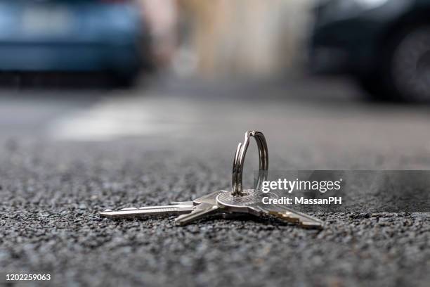 lost home keys with simple keyring on city pavement with blurred cars in the background - lost item stock-fotos und bilder