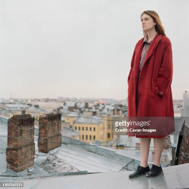 portrait of beautiful brunette woman in red coat standing on the roof - überzieher stock-fotos und bilder