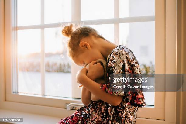 young girl playing with her toy at home in a sparkly dress at sunset - compassionate eye stockfoto's en -beelden