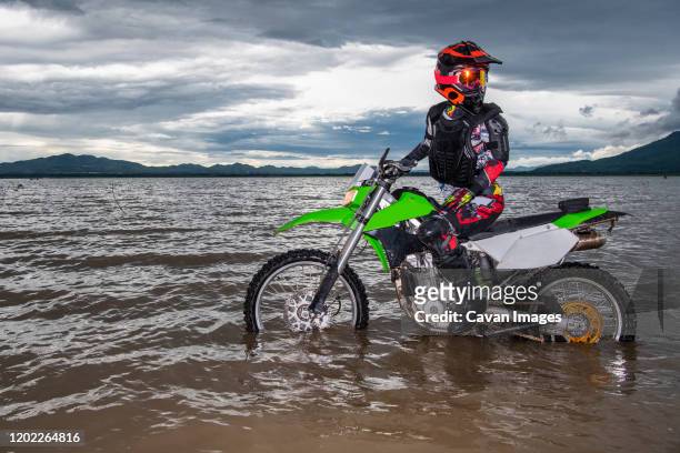 woman standing with her dirt bike in a lake - google ventures stock pictures, royalty-free photos & images