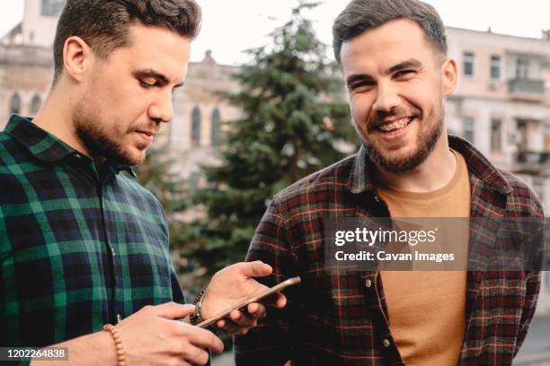 man using smart phone while his brother standing beside him laughing - twins stock pictures, royalty-free photos & images