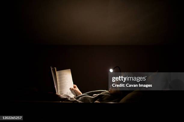 young girl reading before bedtime in bed with lamp - bedtime stock pictures, royalty-free photos & images