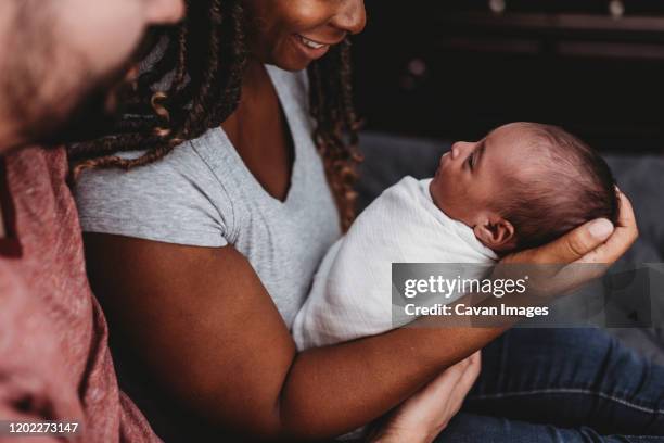 parents smiling at multiracial infant swaddled in white blanket - babydeken stockfoto's en -beelden